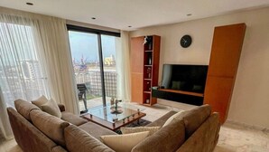 A modern living room with a large sofa, a coffee table, and a TV mounted on the wall.