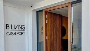 A modern entrance with a glass door, a wooden door frame, and a doormat with "B LIVING CASA PORT" text.