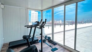 A modern gym with exercise equipment, large windows, and a view of the cityscape.
