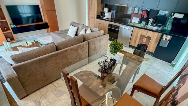 A modern living room with a glass dining table, brown leather sofa, and a TV.