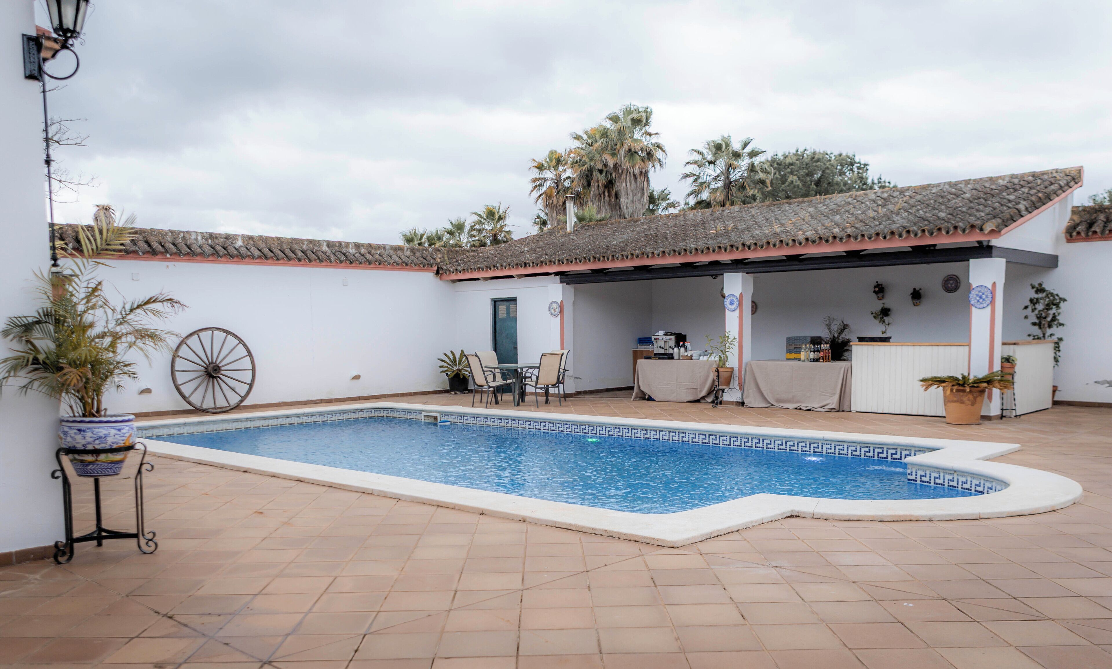 Una piscina con bordeado de baldosas, zona de estar techada y mostrador de recepción.