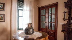 A room with a round wooden table, a pitcher, and a lace doily. There is a door with glass panels and a wooden cabinet to the right.