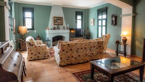 A living room with a fireplace, floral sofas, and a piano.