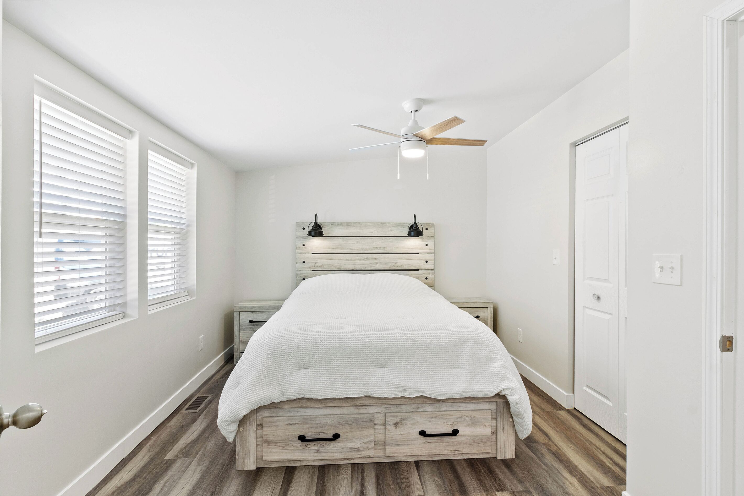 Quarto com cama, ventilador de teto, mesa de cabeceira e porta.