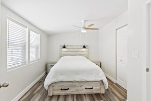 Une chambre à coucher avec un lit, un ventilateur de plafond, une table de chevet et une porte.