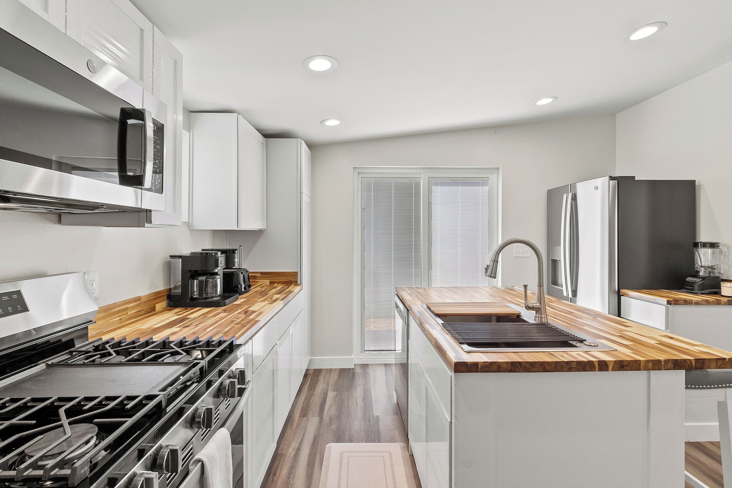 A modern kitchen with white cabinetry, a stainless steel range, a built-in oven, a coffee maker, and a refrigerator.