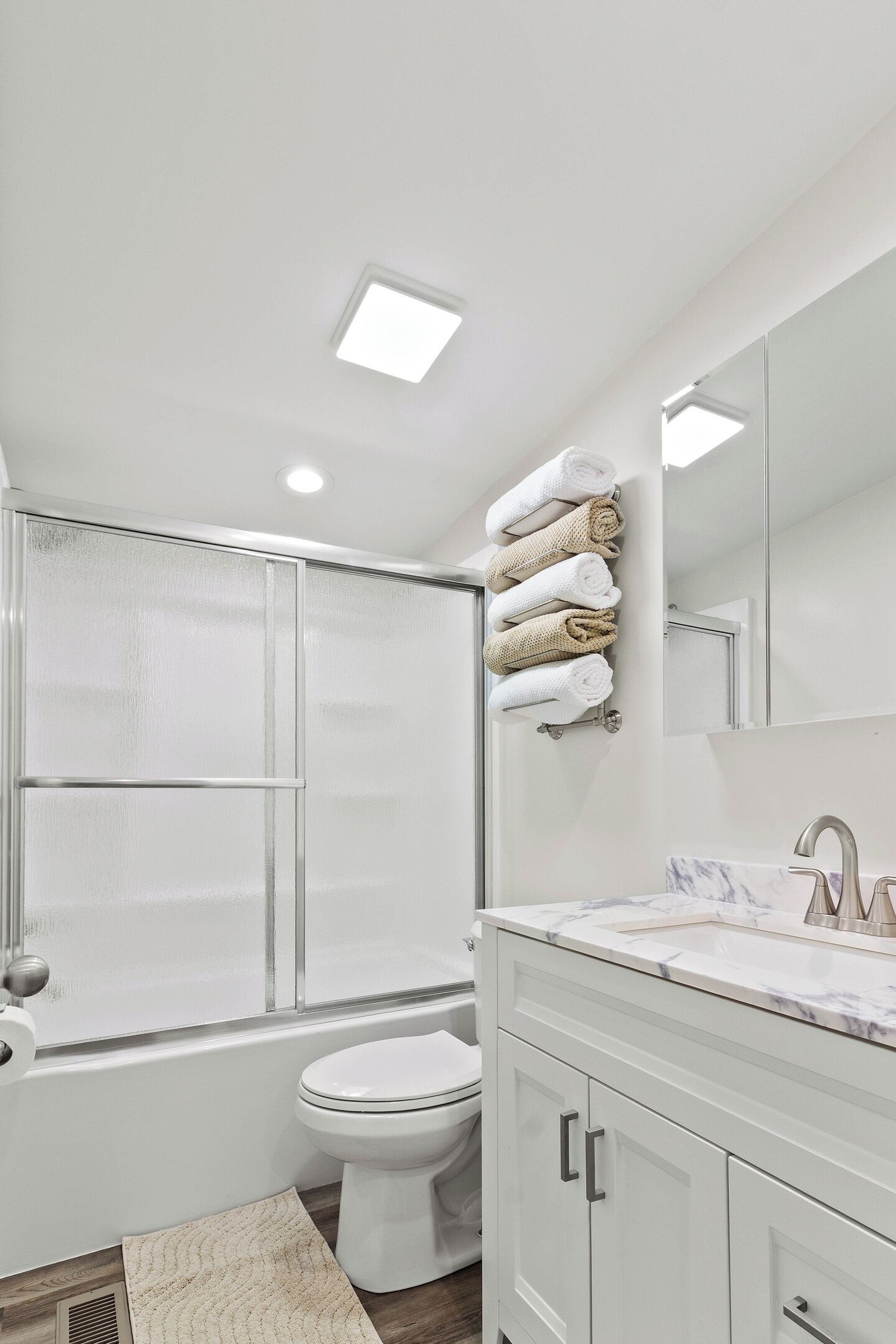 Une salle de bain moderne avec une douche à parois de verre, des toilettes, un lavabo doté d’un plan de travail en marbre, et des serviettes soigneusement pliées et rangées sur un porte-serviettes.