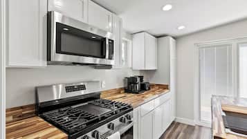 A modern kitchen with stainless steel appliances, a wooden countertop, and a window with blinds.