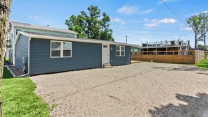 A single-story mobile home with a gravel driveway, a small attached garage, and a fenced backyard. - Waterbury Way - Quiet family retreat with patio! (Russells Point)
