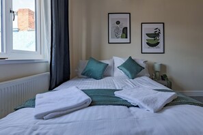 A neatly made bed with white and teal bedding, two framed artworks on the wall, and a window with curtains. - Modern Cozy 2BR- Private Parking- Near WBA (Birmingham)