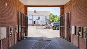 A gated driveway leading to a residential area with a parked car and utility boxes on the walls. - Modern Cozy 2BR- Private Parking- Near WBA (Birmingham)