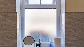 A bathroom with a frosted window, a small shelf with toiletries, and a toilet. - Modern Cozy 2BR- Private Parking- Near WBA (Birmingham)