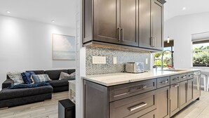 A modern kitchen with dark cabinets, a tiled backsplash, and a large island with a sink. - Casa Blu - Bonita Springs, FL (Bonita Springs)