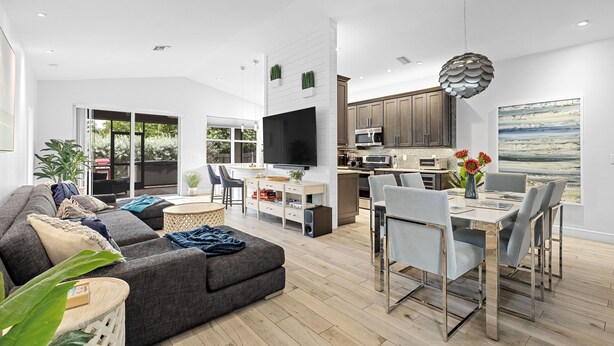 A modern living room with a grey sofa, dining table, and chairs. There is a kitchen area with cabinets and appliances. - Casa Blu - Bonita Springs, FL (Bonita Springs)