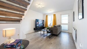 A modern living room with a staircase, a flat-screen TV, a sofa, and a coffee table.