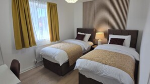 A hotel room with two beds, a desk, and a window with curtains.