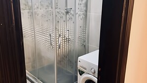 Een moderne badkamer met een douchecabine van glas, een wasmachine en betegelde wanden.