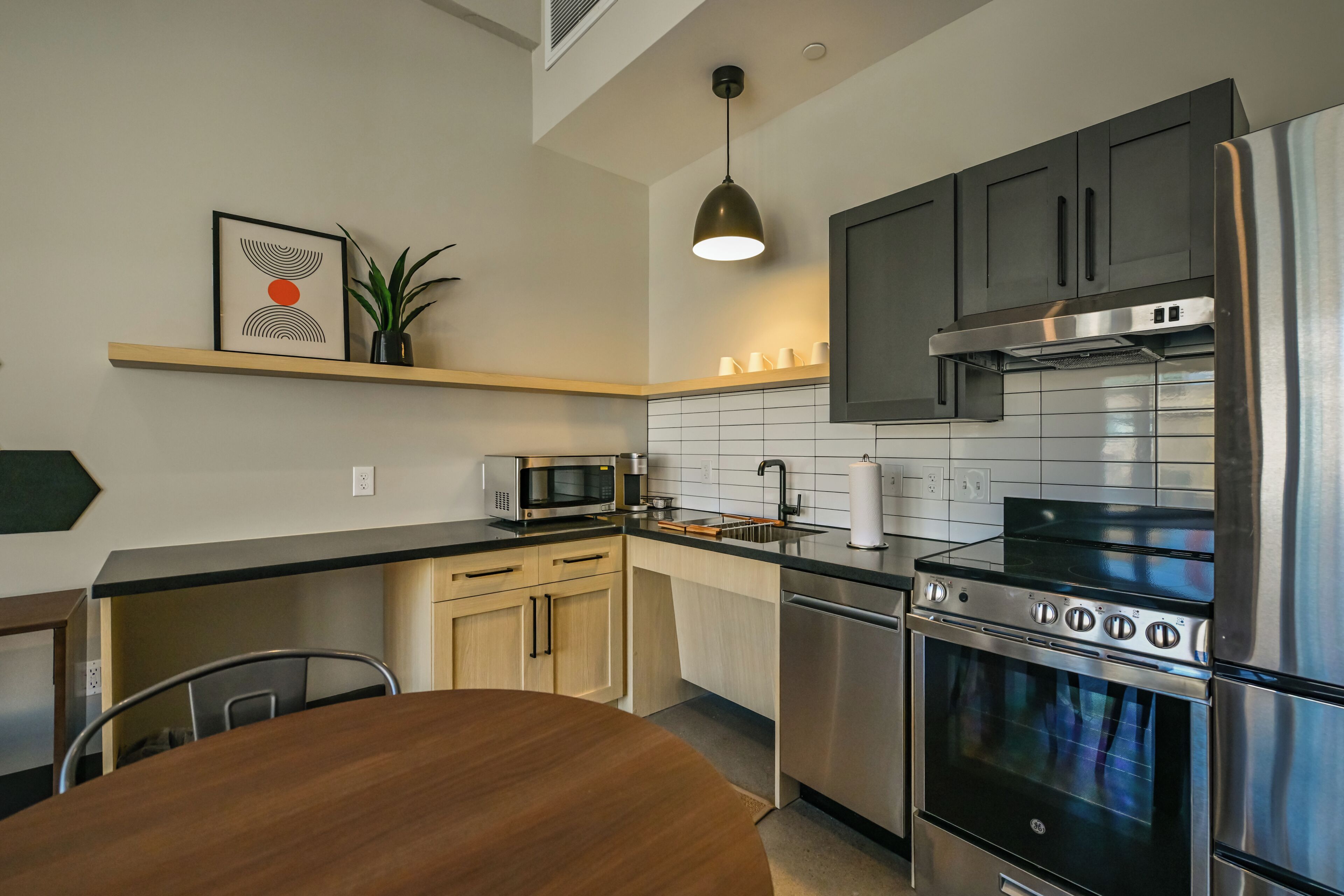 A modern kitchen with a microwave, stove, and dishwasher. There is a wooden dining table and chairs.