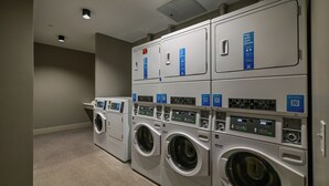 Une laverie équipée de plusieurs machines à laver et de plusieurs séchoirs, dotée de panneaux de commande numériques et affichant les modalités de paiement.