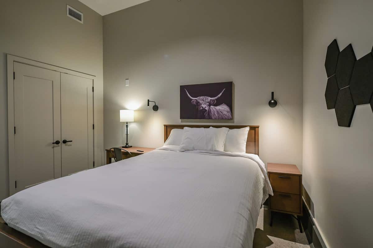 A bedroom with a large bed, a nightstand, a lamp, a wall-mounted artwork of a bull, and a wardrobe.