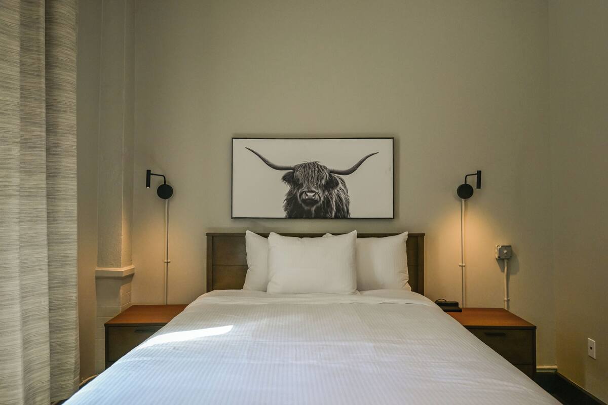 A hotel room with a large bed, two bedside tables, a headboard, a wall-mounted artwork of a bull, and two wall-mounted lamps.