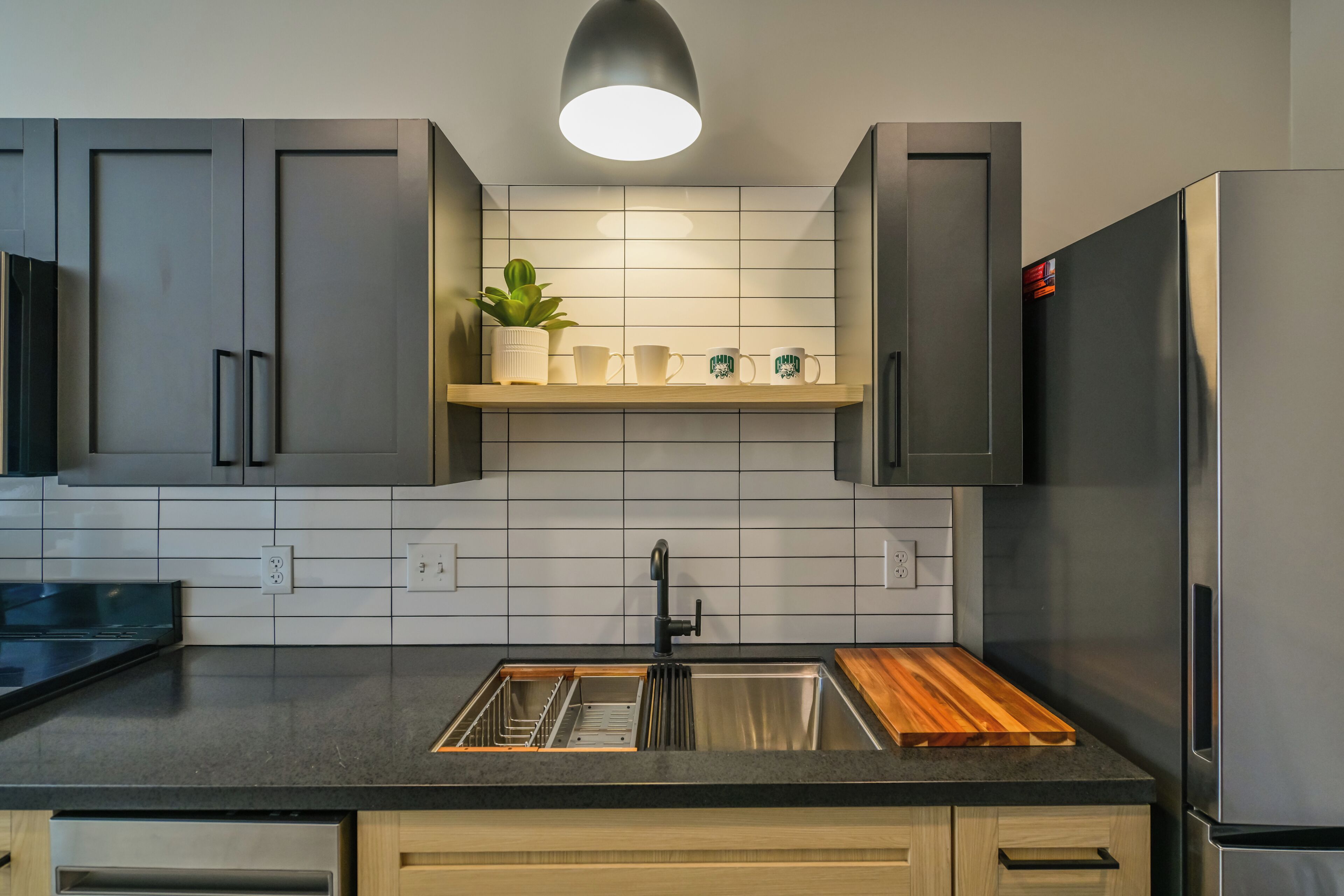A modern kitchen with grey cabinets, a stainless steel refrigerator, a wooden countertop, and a built-in sink.
