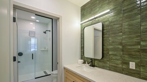 Une salle de bain moderne avec une douche à parois de verre, un lavabo blanc et un mur recouvert de carreaux verts.