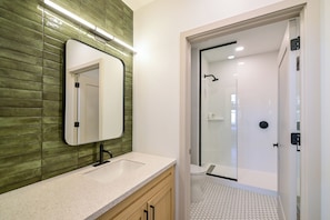 Un baño con espejo, lavamanos y zona de ducha.