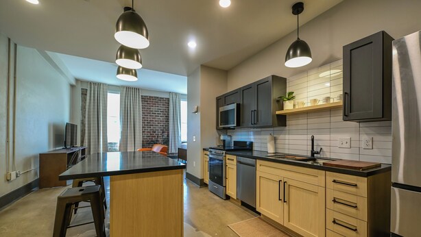 Une cuisine moderne dotée d’un îlot central, d’appareils électroménagers en acier inoxydable et de luminaires suspendus.