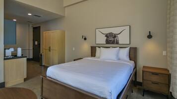 A hotel room with a bed, bedside table, a small desk with a chair, a wardrobe, and a picture of a bull on the wall.