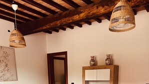 Una sala de estar con un sofá color beige, dos sillas blancas, un mueble de madera y una lámpara colgante de fibras.