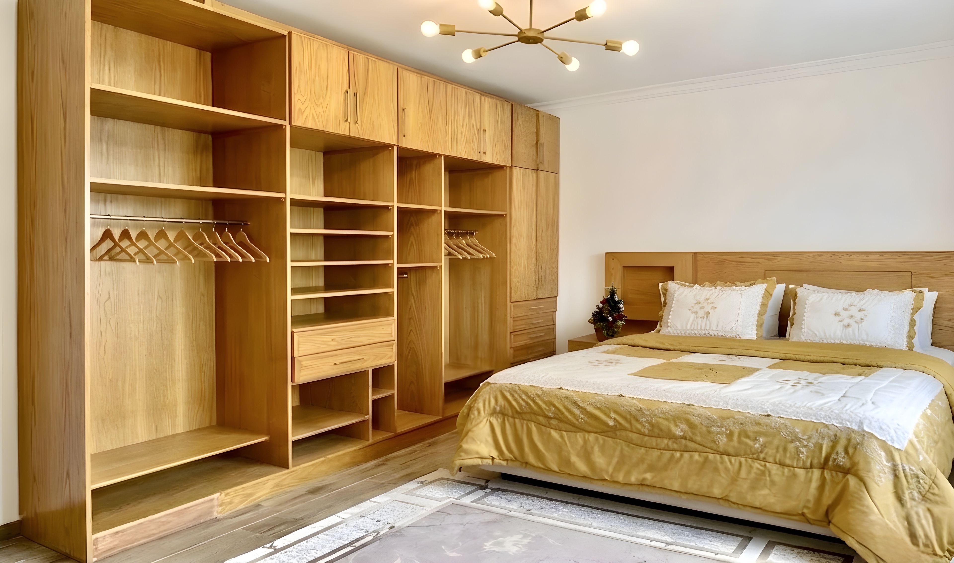 A bedroom with a large wooden wardrobe, a bed with a gold bedspread, and a ceiling light fixture.