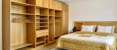 Un dormitorio con un amplio armario de madera, una cama con cubrecama dorado y una lámpara en el techo.