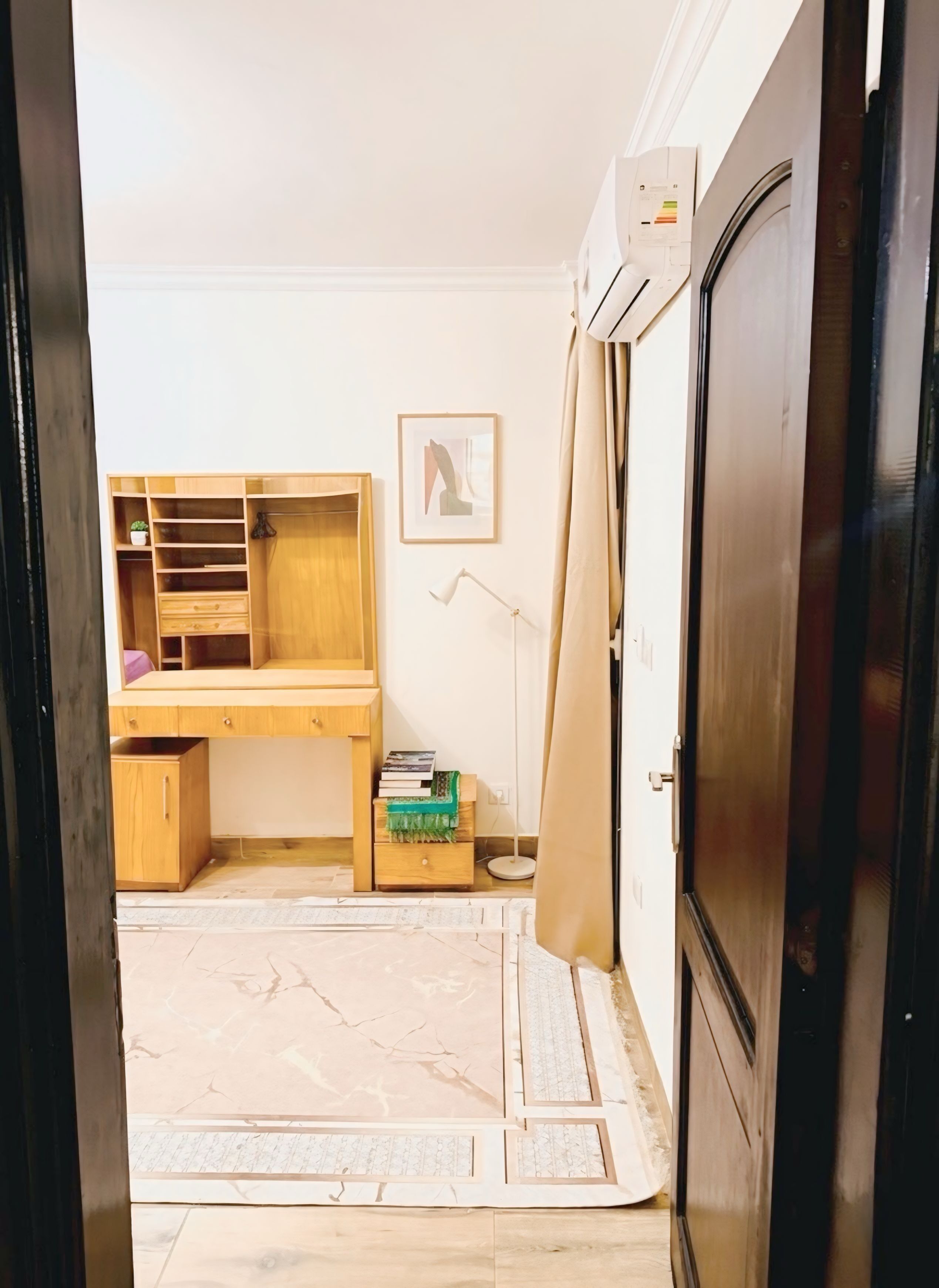 A room with a wooden desk, a standing lamp, a framed picture on the wall, and a wardrobe.