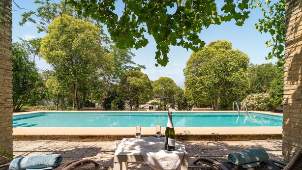 A swimming pool with a table and chairs, surrounded by trees and a brick wall.