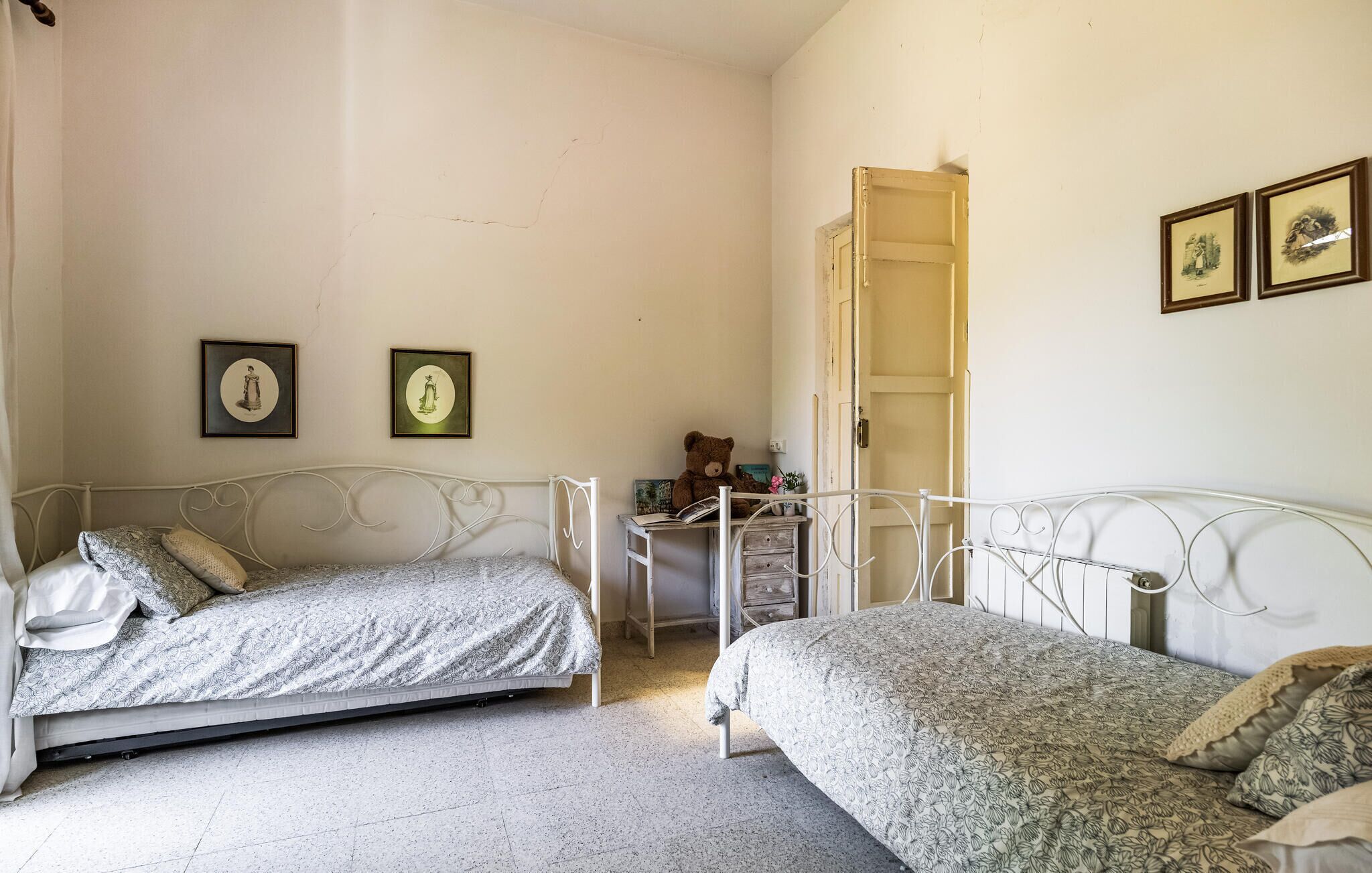 A bedroom with two beds, a small desk, and a door leading to another room.