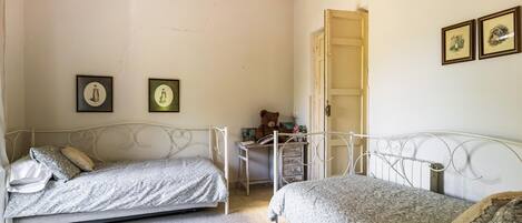A bedroom with two beds, a small desk, and a door leading to another room.