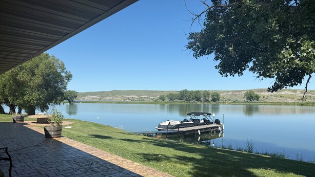 En patio ved søen med en båd i vandet, omgivet af træer og en græsplæne.