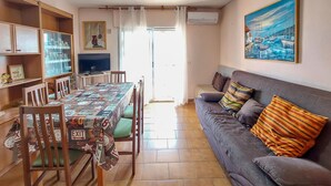 Una sala de estar con un sofá, una mesa de comedor con sillas, un televisor y un cuadro en la pared.