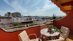 Un balcón con una mesa y sillas, con vista a una zona residencial con casas y cielo despejado.