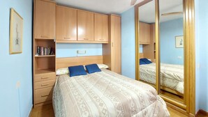 Un dormitorio con cama, armario, espejo y estante con libros.