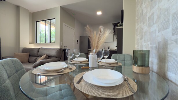 Un comedor moderno con una mesa de vidrio, individuales tejidos y platos blancos.