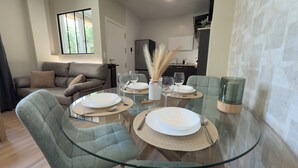 Un comedor con mesa de vidrio dispuesta para cuatro personas, rodeado de sillas tapizadas en verde.