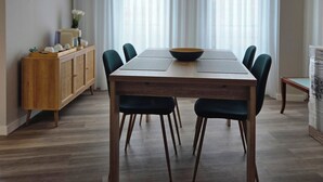 A dining area with a wooden table, chairs, a hanging light fixture, and a window with curtains.