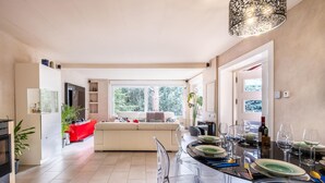 A modern kitchen with a dining area, large windows, and a sofa in the background.