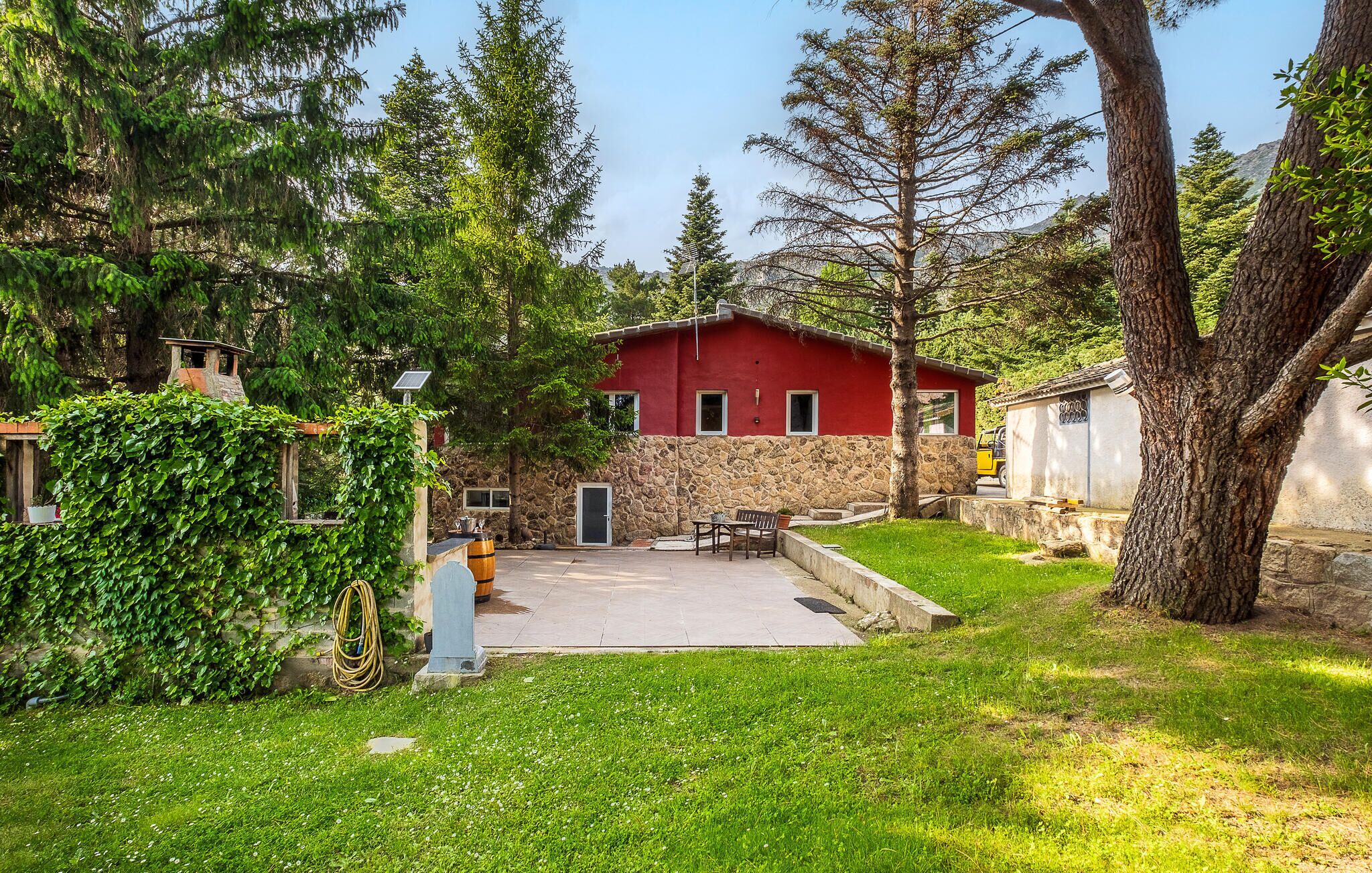 A red building with stone walls, a paved patio, and a grassy yard.