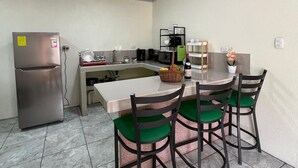 Een kleine keuken met een koelkast, een spoelbak en een eethoek met vier stoelen.