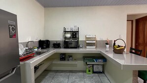 Een kleine keuken met een koelkast, gootsteen en magnetron. Er zijn kastjes en een aanrecht met diverse spullen.