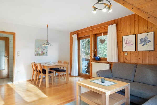 A wooden-paneled room with a dining table, chairs, a sofa, and a small table with a cup.