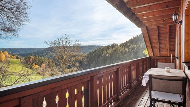 A wooden balcony with a table and chair, overlooking a mountainous landscape. - Apartment 'Wiesenblick' with Shared Terrace, Shared Garden and Wi-Fi (Schramberg)